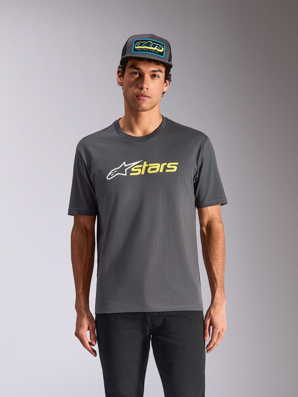 Alpinestars Blaze 2.0 CSF Tee, Short Sleeve T-Shirt, Charcoal Gray, White star logo and Hi-Vis Yellow stars graphic, worn with matching trucker hat and black pants, casual motorsport streetwear