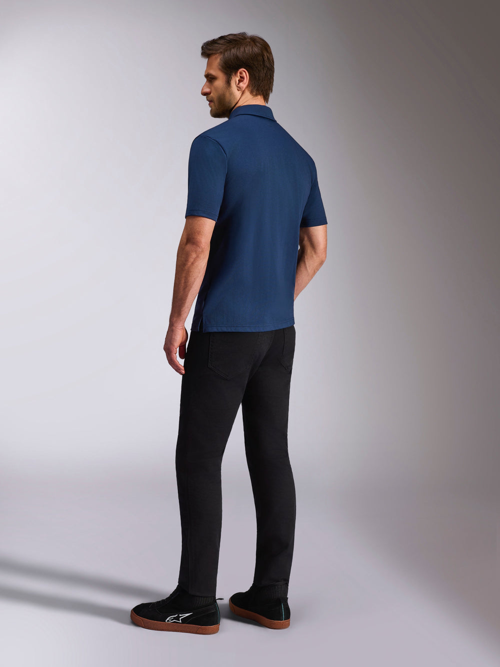 Alpinestars Impetus Sport Polo, Navy Blue Short Sleeve Polo Shirt, Back and side view on model, paired with black pants and black sneakers, casual motorsport lifestyle sportswear