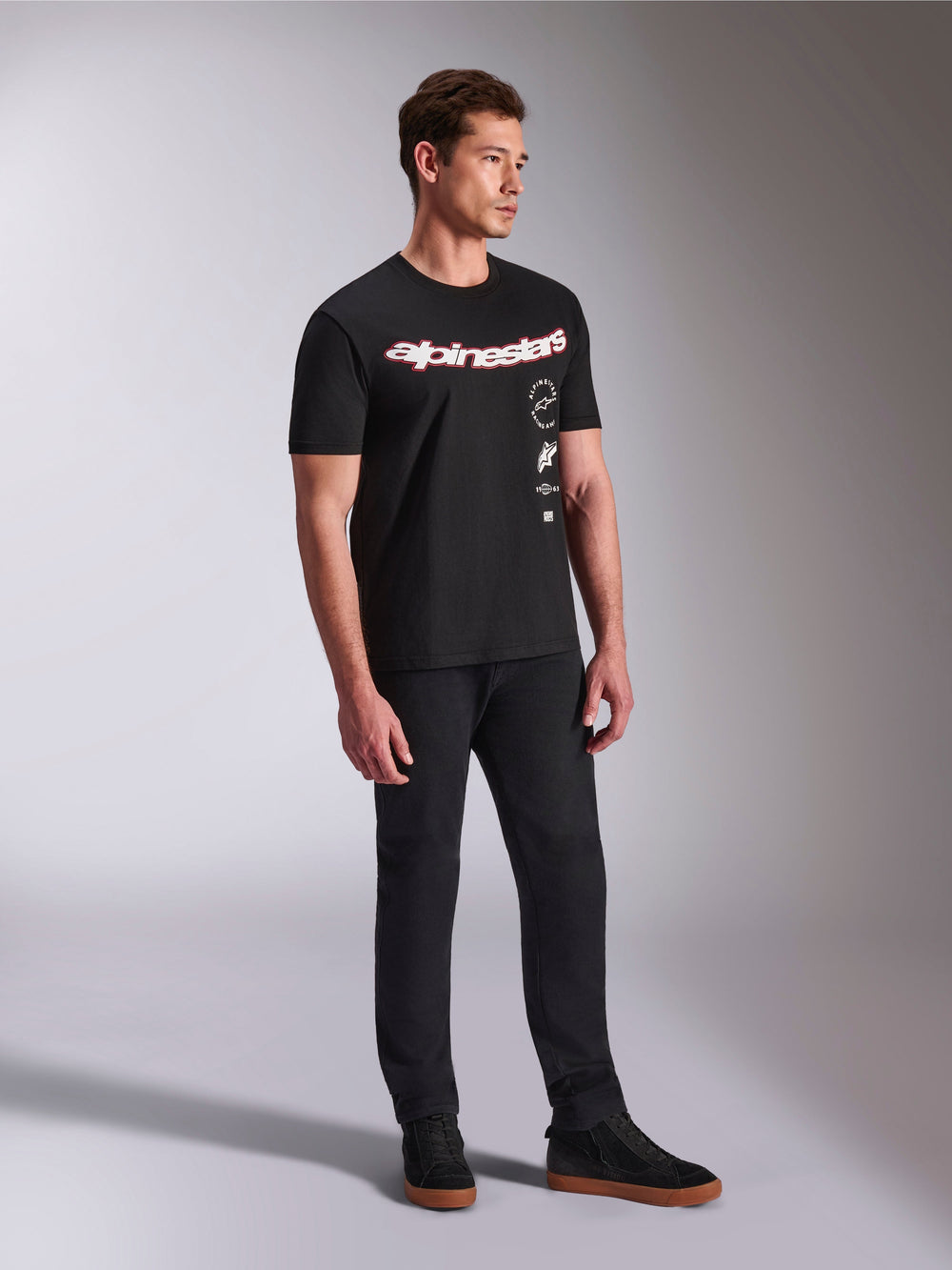 Alpinestars Abus CSF Tee, Short Sleeve T-Shirt, Black, featuring curved red and white Alpinestars logo with vertical stacked graphics, worn with black pants and sneakers, casual motorsport-inspired streetwear