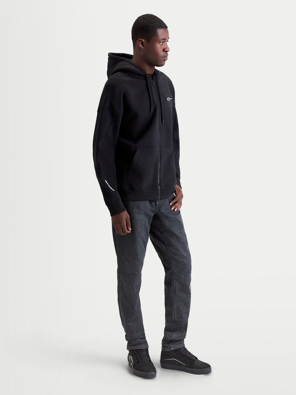 Alpinestars Entity Oversized Hoodie, Sportswear Zip-Front Fleece, Black, 80% Cotton and 20% Recycled Polyester. Features include a Vislon front zipper, kangaroo pocket, and embroidered logo on the chest and sleeve. Shown on model for a relaxed, oversized fit, ideal for casual motorsport style.