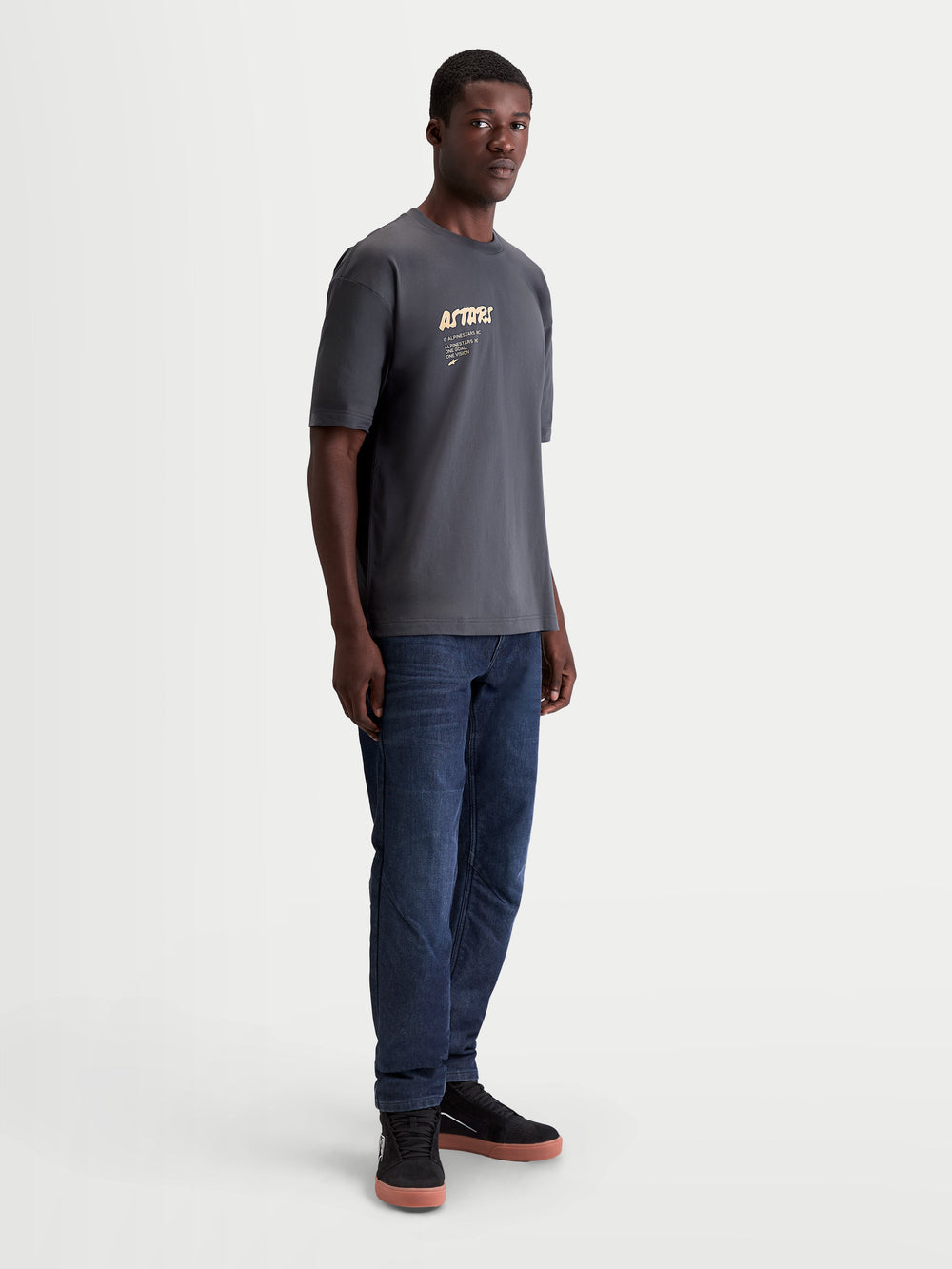 Alpinestars Chalk Oversized CSF Tee, Men's Short Sleeve Sportswear T-Shirt, Charcoal Gray, featuring a relaxed oversized fit and a soft-hand Astars chest graphic. This 60/40 cotton-poly blend casual tee is shown on a model, ideal for everyday motorsport-inspired style.