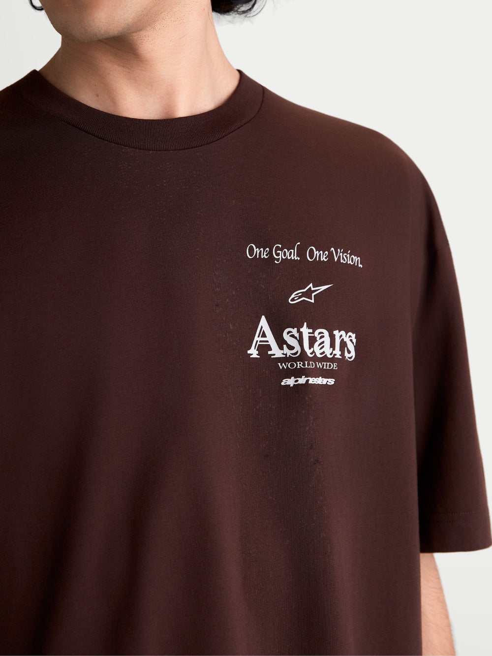 Alpinestars Post Oversized CSF Tee, Short Sleeve Sportswear T-Shirt, Brown and White, close-up of chest branding featuring 'One Goal. One Vision.' and Astars Worldwide graphics, soft cotton blend, worn by model for casual motorsports lifestyle.