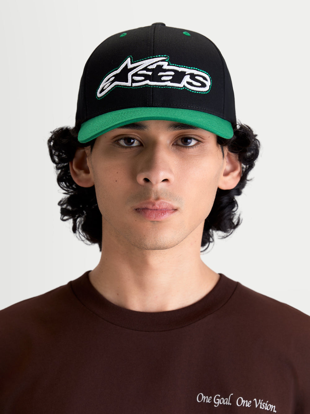 Alpinestars Retro Snapback Hat, Sportswear Lifestyle Cap, Black and Green, featuring a curved bill, structured crown, and front embroidered Astars logo with green running stitch, shown on model front view.