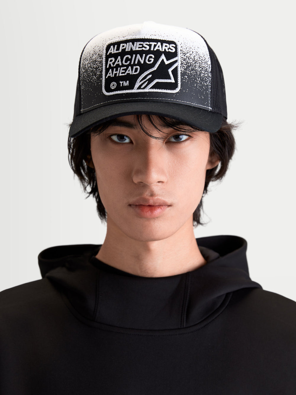 Alpinestars Gravel Trucker Hat, Sportswear Lifestyle Cap, Black and White, On-Model Front View featuring a Curved Bill, Breathable Mesh Back, and Racing Ahead Woven Patch with Gravel Texture Detailing.