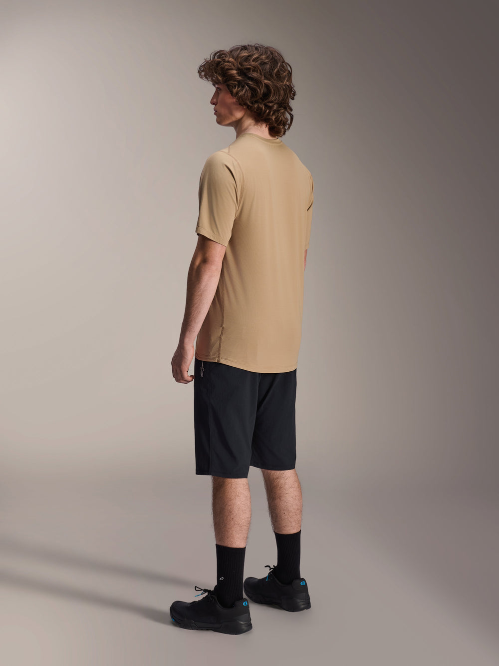 Alpinestars A-Dura Liner Shorts in Black and A-Dura SS Jersey in Tan, worn by a male model from a side profile view, paired with black socks and cycling shoes, mountain bike lifestyle apparel.