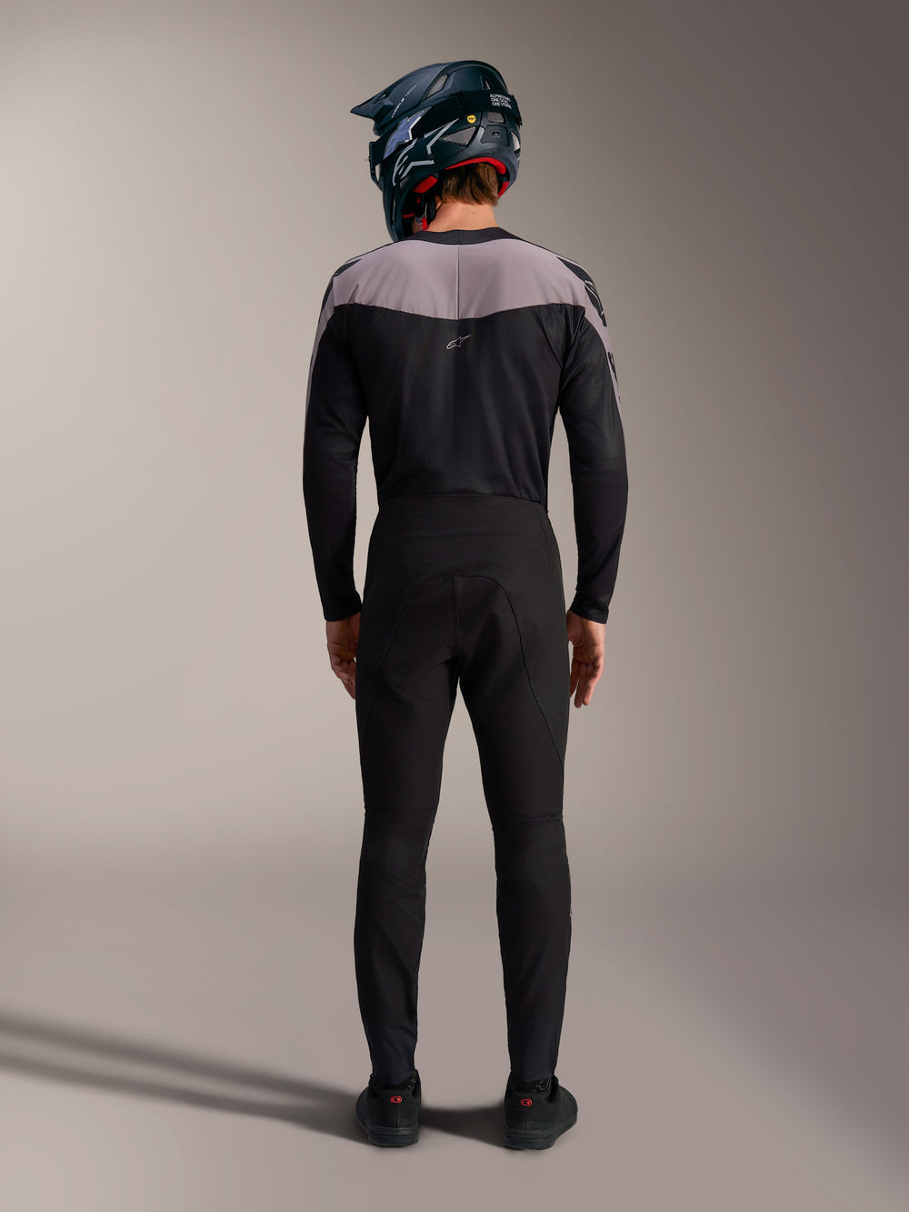Alpinestars A-Supra Elite MTB kit in black, featuring performance pants and jersey with a full-face helmet, back view.