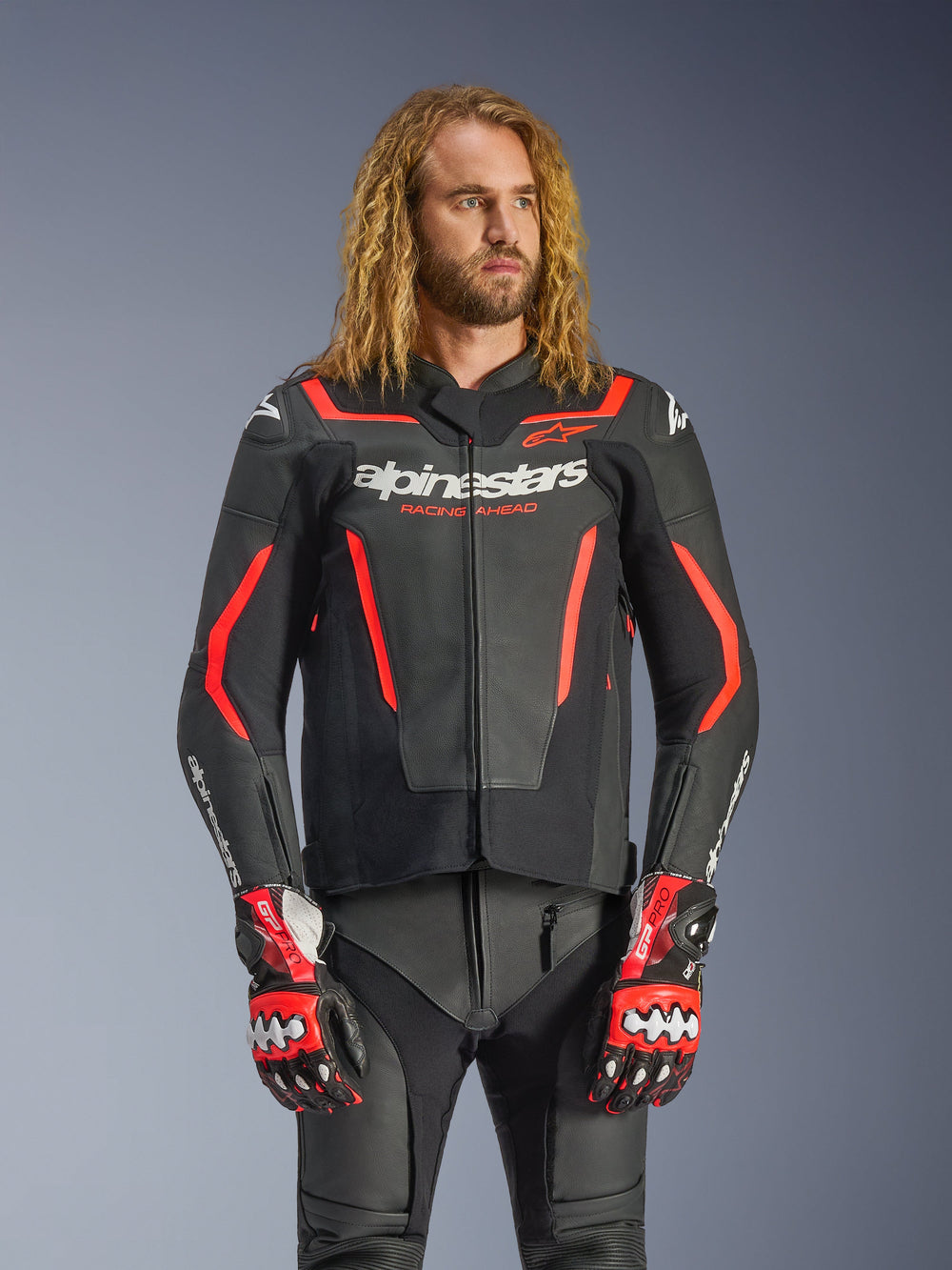 Alpinestars GP Force V2 Leather Jacket, Sport Motorcycle Jacket, Black and Red Fluo, worn by a male model with long wavy hair, featuring white Alpinestars logo and 