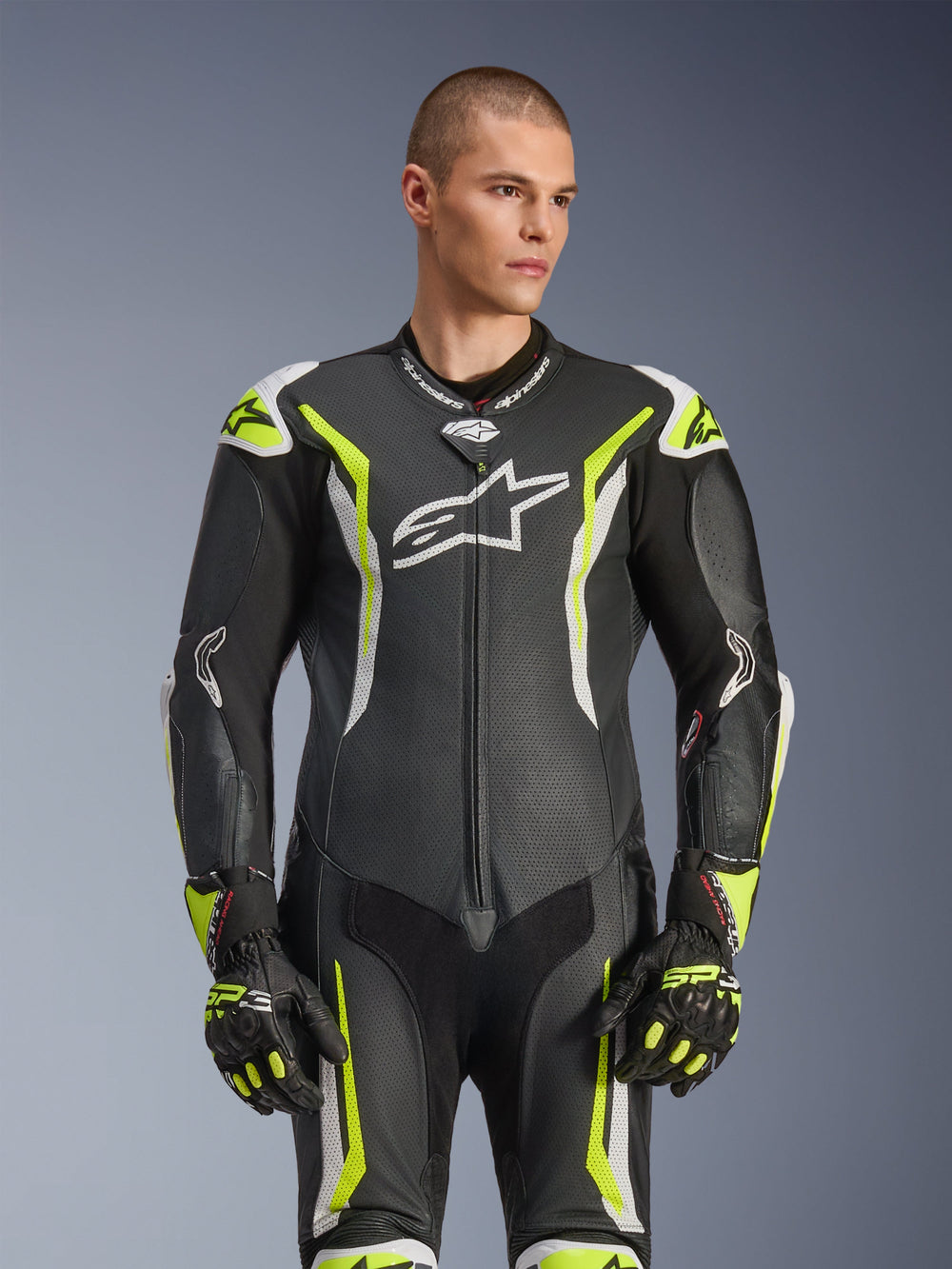 Alpinestars GP Tech V5 One Piece Leather Suit, Black White and Yellow Fluo, professional racing gear, perforated leather with large white Astar logo on chest, fluorescent yellow and white accents, worn with matching racing gloves