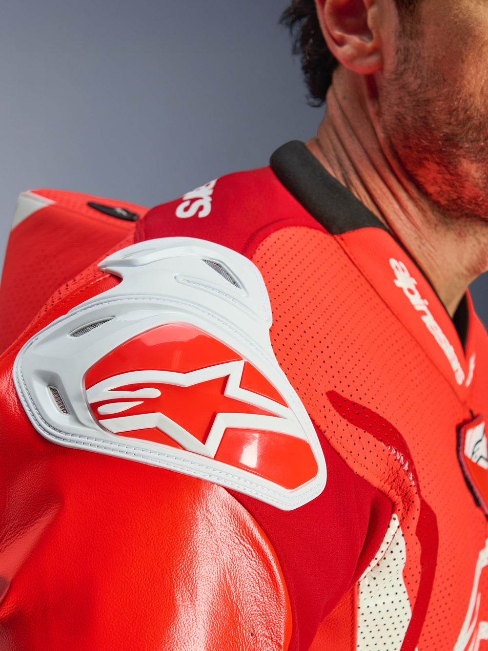 Close-up of the shoulder area on the Alpinestars GP Tech V5 One Piece Leather Suit, Red Fluo and Bright Red, featuring a white GP DFS impact shield with a red star logo and perforated leather for ventilation.