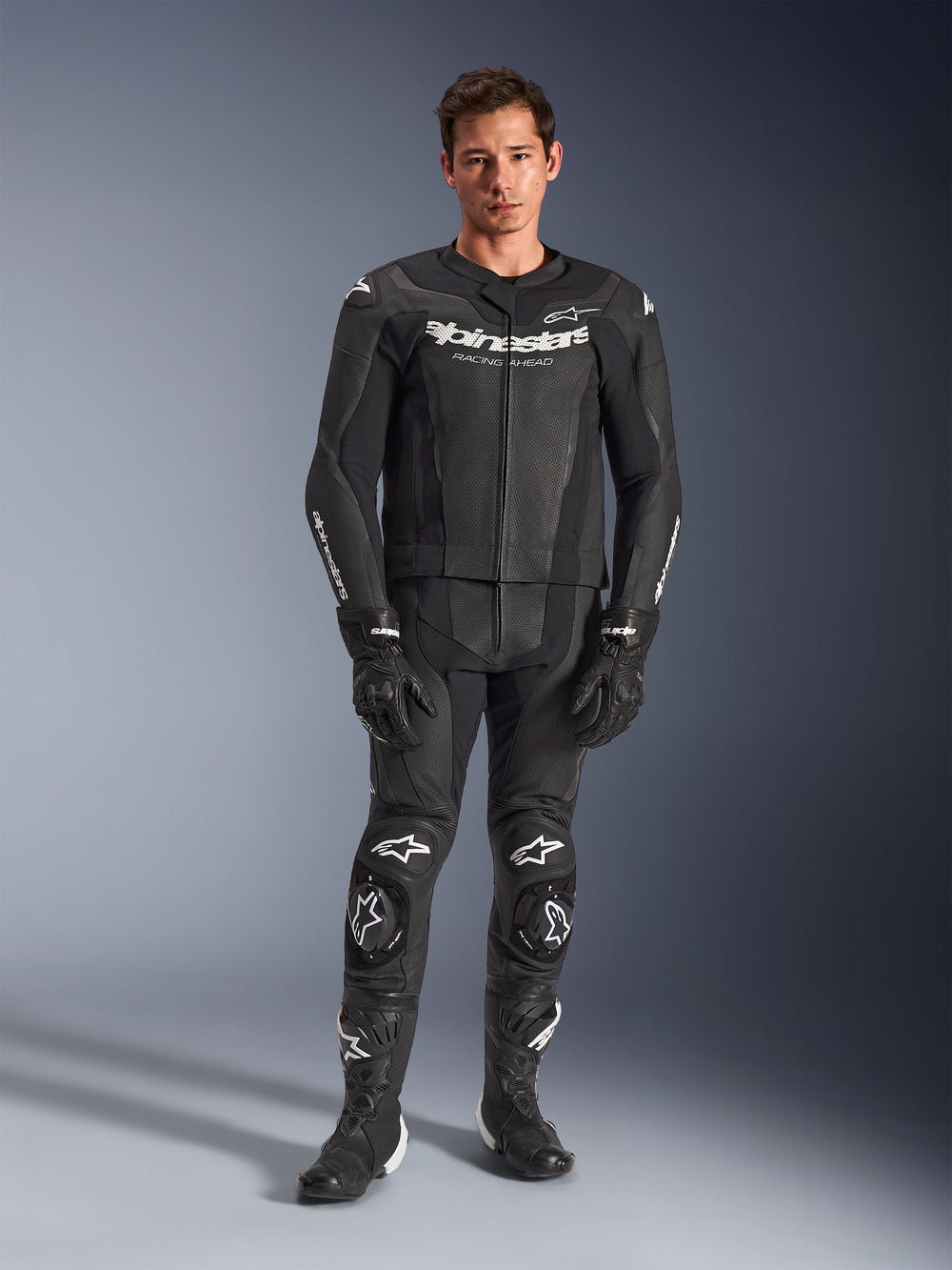 Alpinestars GP Force V2 Leather Suit 2-Piece, Black with white logos, full-body motorcycle racing suit, featuring premium leather construction with reinforced knee sliders and perforated panels, worn with black gloves and boots, studio full-length view