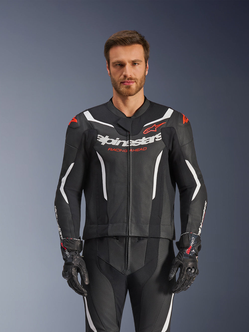 Alpinestars GP Force V2 Leather Suit- 2Piece, Black White and Red Fluo, front view of male model wearing the perforated leather suit with matching black gloves, featuring white angular accents and Alpinestars branding on the chest