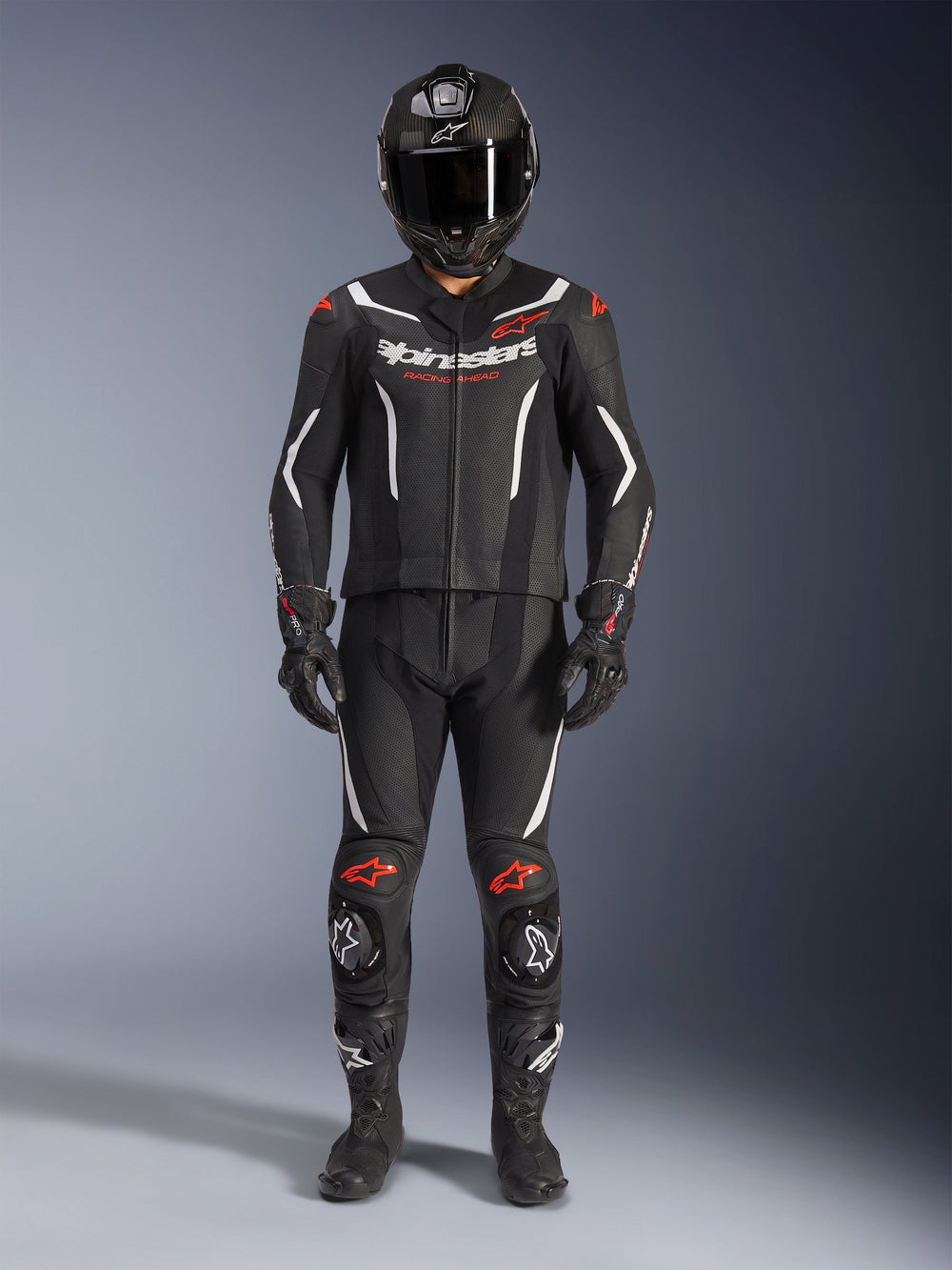 Alpinestars GP Force V2 Leather Suit 2-Piece, Motorcycle Racing Suit, Black White and Red Fluo, featuring white Alpinestars logo on chest and red accents on shoulders and knees, worn with black full-face helmet, black gloves, and black boots for a complete performance gear set