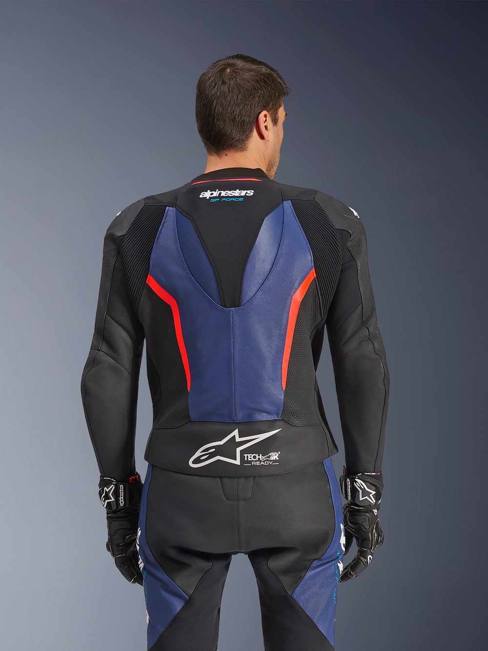 Alpinestars GP Force V2 Leather Suit 2-Piece, Back view, Black with Blue and Red Fluo accents, featuring perforated leather construction, Tech-Air Ready branding on the waist, and ergonomic stretch panels for racing performance.