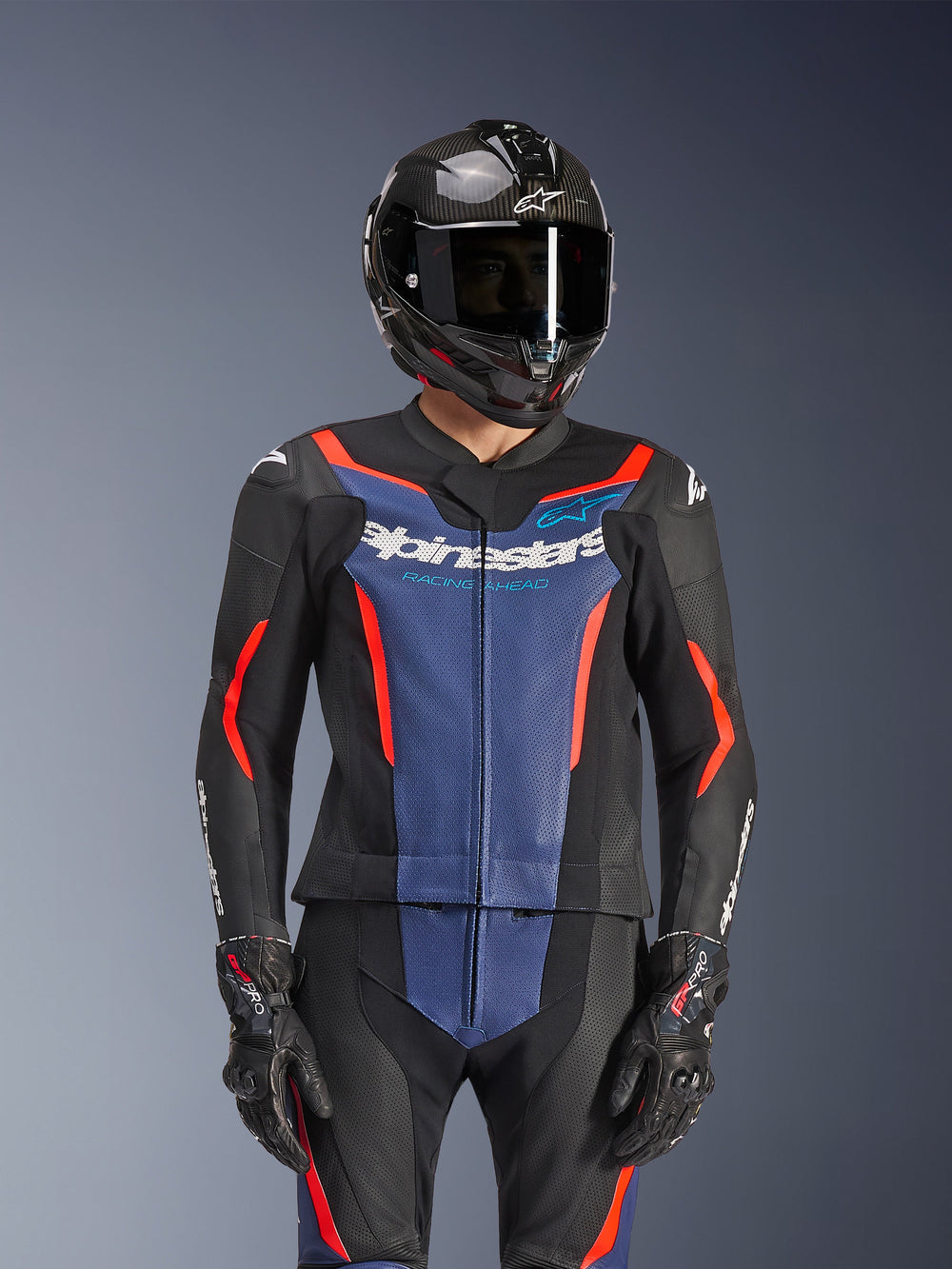 Alpinestars GP Force V2 Leather Suit 2-Piece, Black Blue and Red Fluo, worn with a carbon fiber helmet and racing gloves, featuring perforated leather panels and white Alpinestars logo on the chest, professional racing and sport riding gear