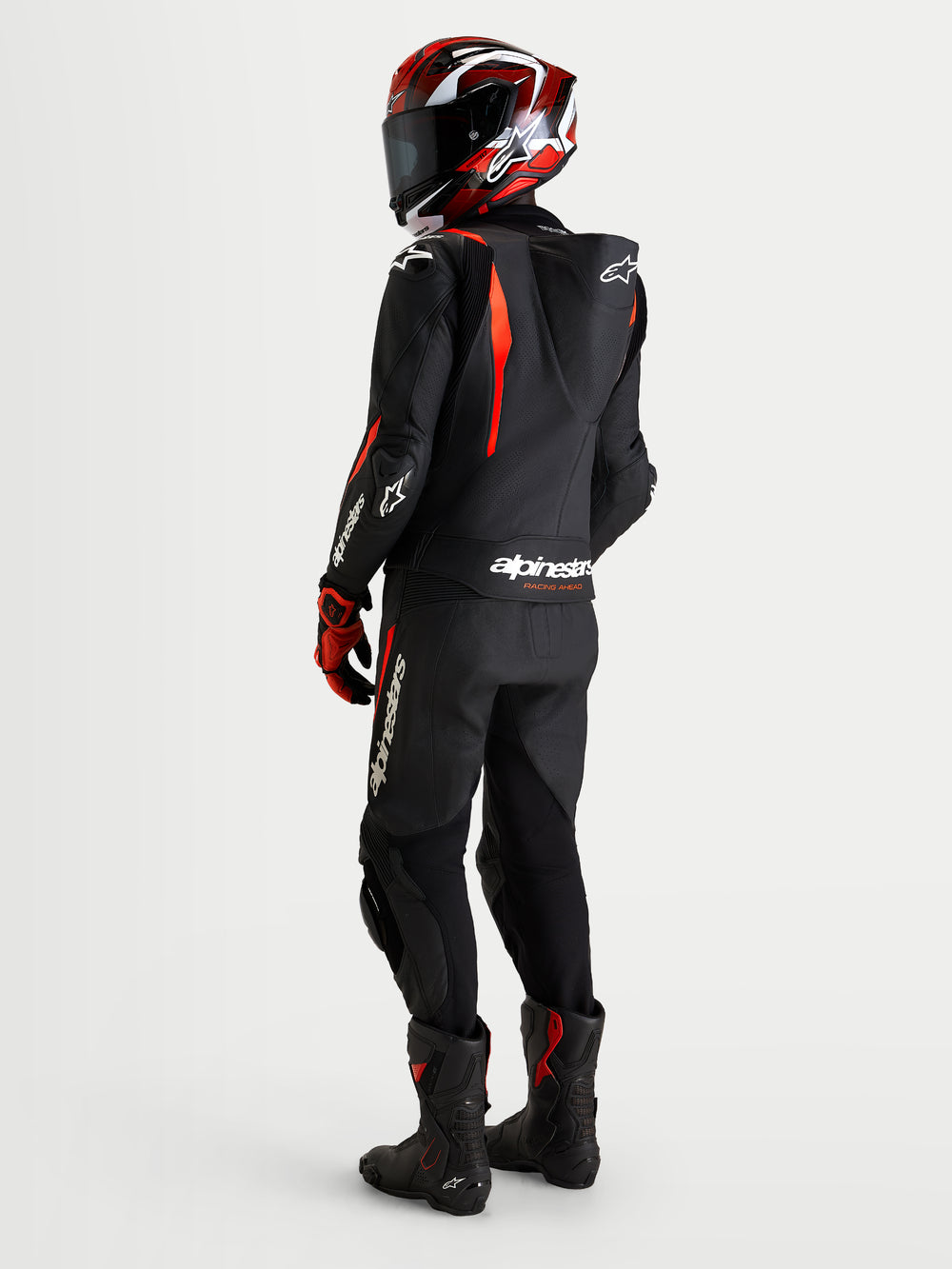 Alpinestars Missile V3 Leather Suit 2 Piece, Black and Red Fluo, men's motorcycle racing suit worn with a helmet, showing rear view with aerodynamic speed hump and AAA abrasion protection