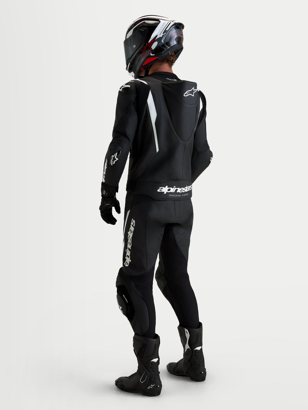 Alpinestars Missile V3 Leather Suit 2 Piece, Black and White, rear view of a rider wearing a professional motorcycle racing leather suit with aerodynamic speed hump, DFS shoulder and knee protection, and matching helmet