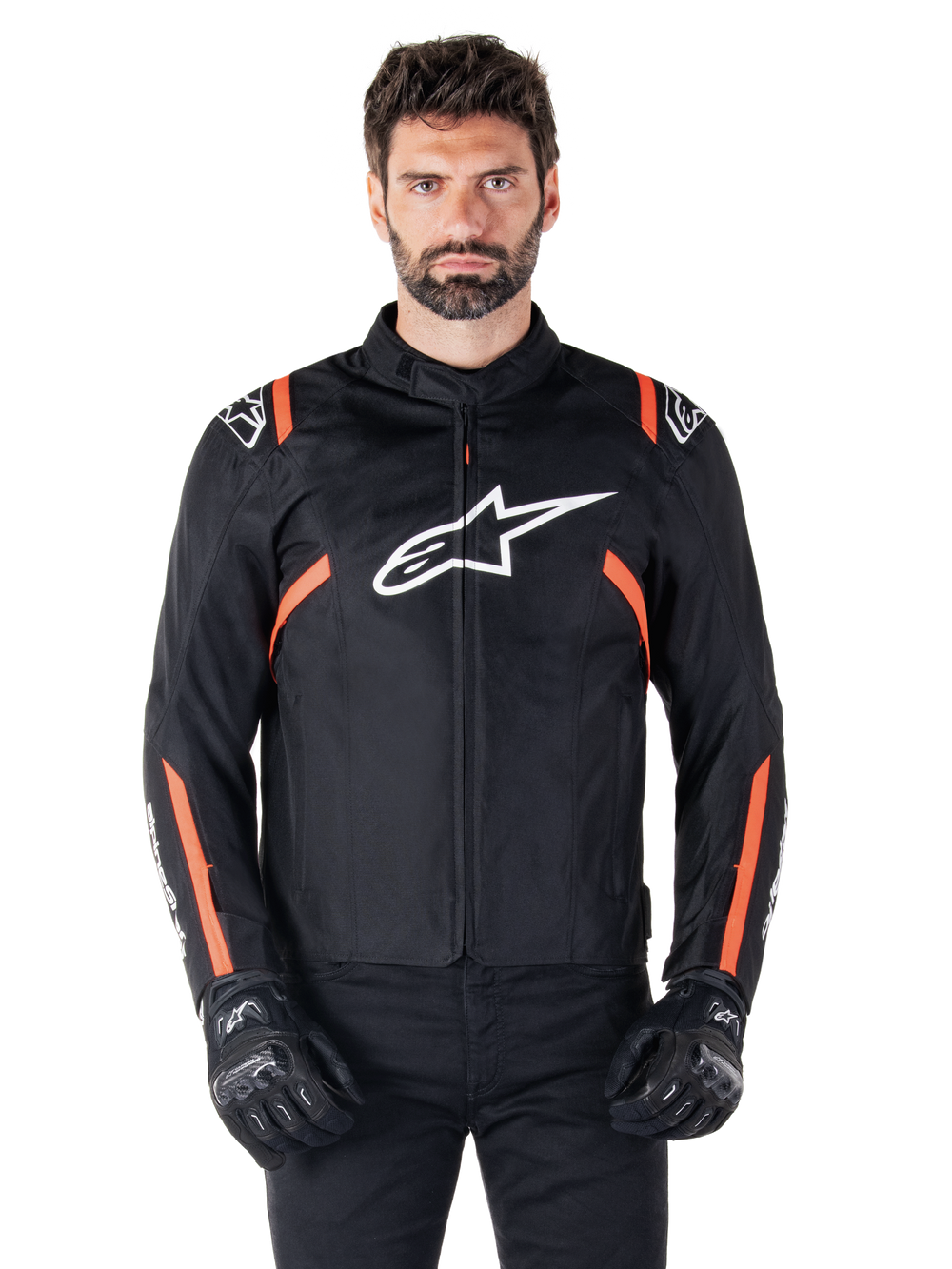 Alpinestars T-SPS V2 Waterproof Jacket, Black White and Red Fluo, worn by a male model with black riding gloves, featuring a large white Alpinestars logo on the chest and vibrant orange accents on the shoulders and sleeves.