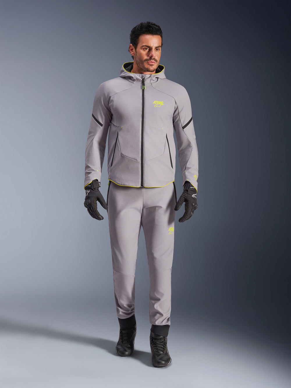 Alpinestars Aeroshell Waterproof Jacket, Mid Gray Yellow Fluo, worn with matching gray pants, black gloves and boots, featuring a modern sport-inspired hoodie design with vibrant yellow accents and athletic fit.