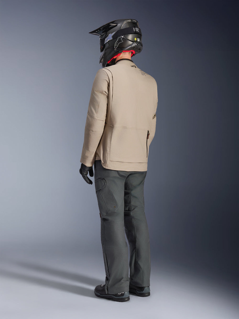 Alpinestars Borrego Drystar® Jacket, Warm Gray adventure motorcycle jacket, back view of rider wearing dark gray pants and a black helmet, featuring a rugged waxed-canvas look and functional design.