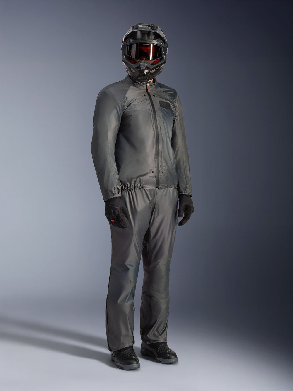 Rider wearing the Alpinestars Borrego Drystar® Jacket in Warm Gray, full-body adventure gear with matching gray pants, black full-face helmet with goggles, and black gloves, featuring a sleek waterproof textile design.
