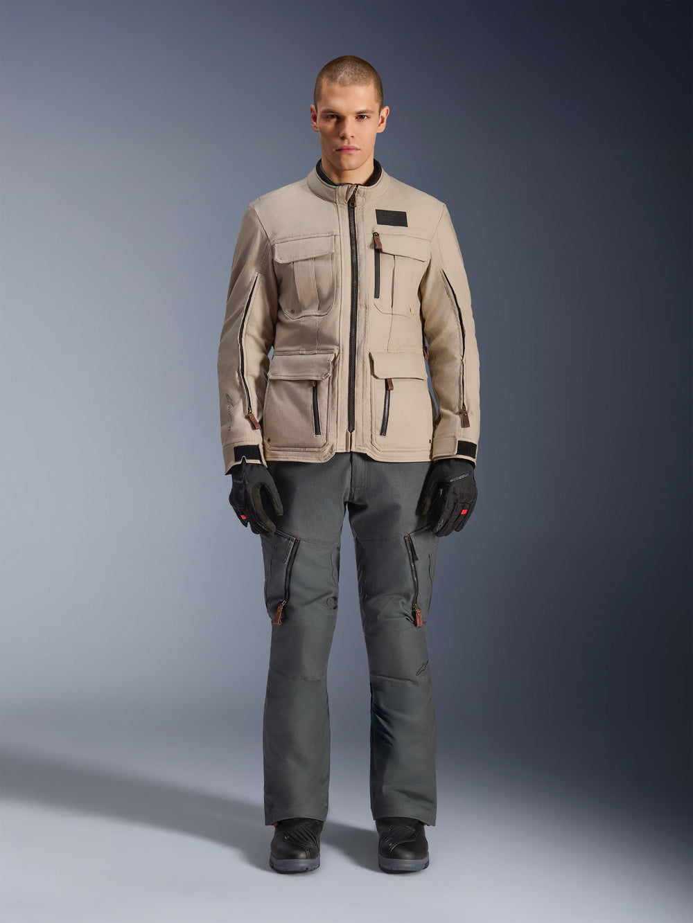 Alpinestars Borrego Drystar® Jacket, Adventure Motorcycle Jacket, Warm Gray, worn by a model with dark gray riding pants and black gloves, featuring multiple cargo pockets and a durable textile construction with a classic waxed-canvas look.