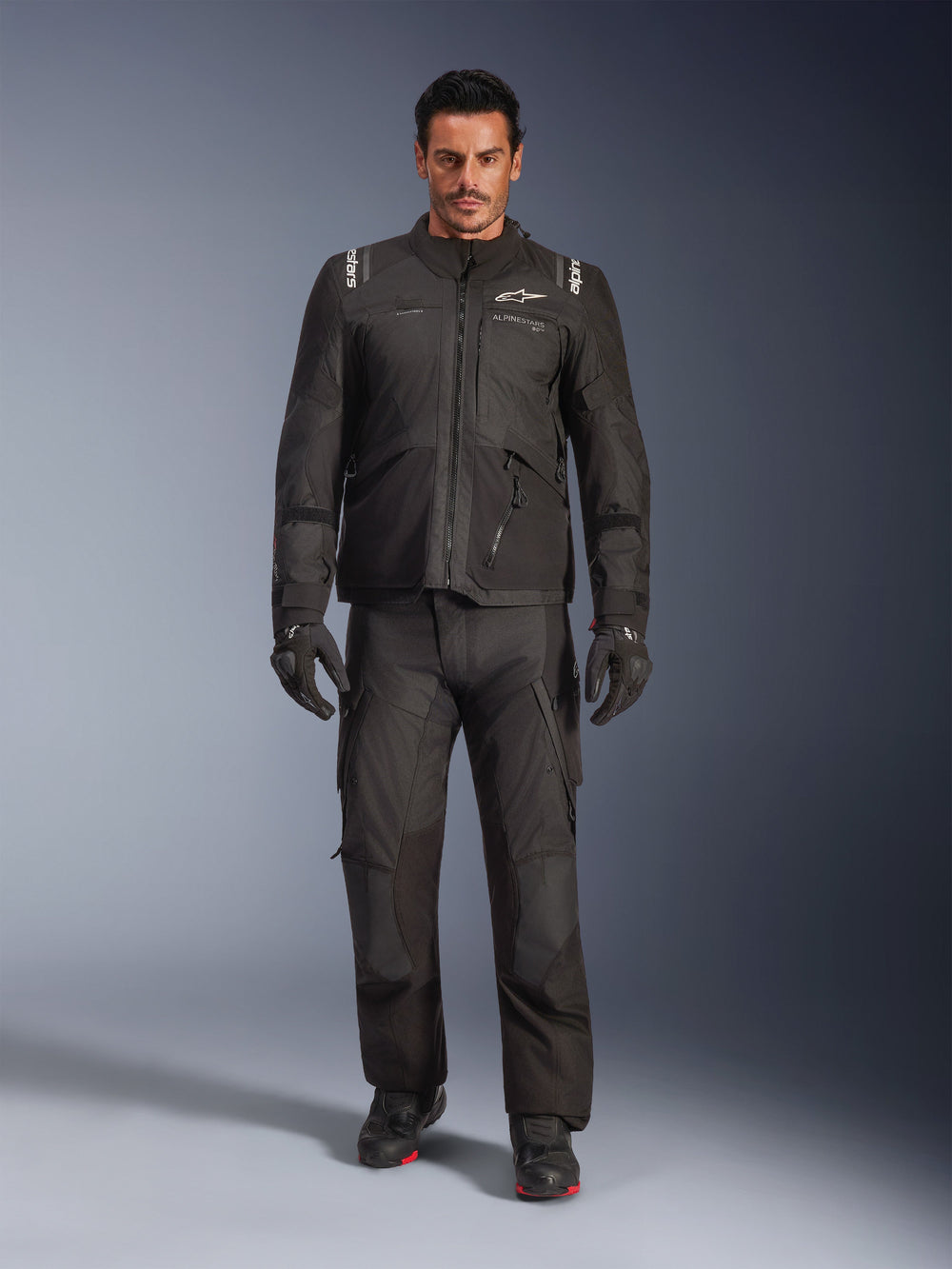 Male model wearing the Alpinestars Andes V4 Drystar® Jacket in Black, paired with matching adventure motorcycle pants, black gloves, and black boots, full-body studio shot showcasing technical all-weather touring gear with Alpinestars branding.