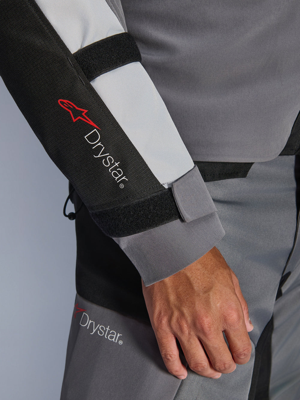 Close-up of Alpinestars Andes V4 Drystar® Jacket sleeve, Dark Gray and Ice Gray with Black accents, featuring Drystar® logo and adjustable forearm straps, part of a waterproof textile adventure motorcycle outfit