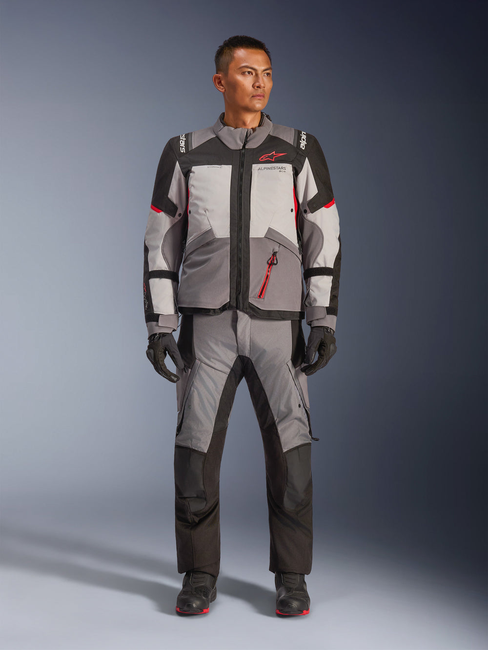 Alpinestars Andes V4 Drystar® Jacket, Motorcycle Adventure Jacket, Dark Gray, Ice Gray, Black, and Bright Red, worn with matching textile riding pants and gloves, featuring a technical multi-panel design with a red Alpinestars logo, adventure-touring gear.