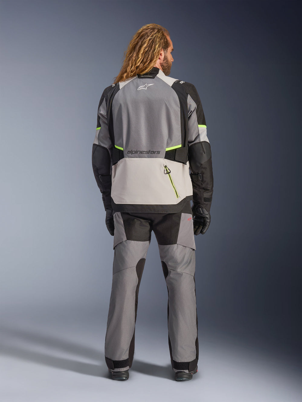 Alpinestars Andes V4 Drystar® Jacket, Adventure Motorcycle Jacket, Dark Gray and Ice Gray with Black and Yellow Fluo accents, rear view worn with matching pants and black gloves, featuring a large back pocket with yellow zipper and reinforced shoulder and elbow panels