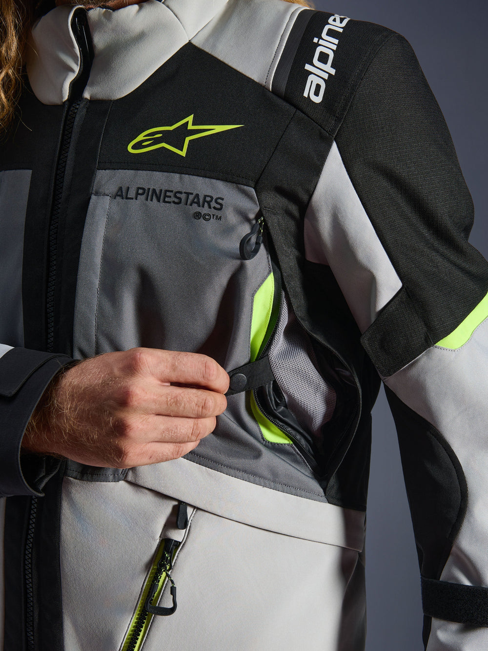 Alpinestars Andes V4 Drystar® Jacket, Motorcycle Jacket, Dark Gray/Ice Gray/Black/Yellow Fluo, close-up detail showing a hand opening the chest ventilation intake with neon yellow accents and mesh lining, durable textile construction with Alpinestars branding.
