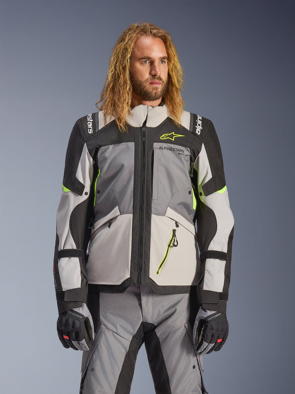 Alpinestars Andes V4 Drystar Jacket, Adventure Touring Motorcycle Jacket, Dark Gray and Ice Gray with Neon Yellow accents, worn by a model with matching pants and gloves, multi-pocket textile design for all-weather riding