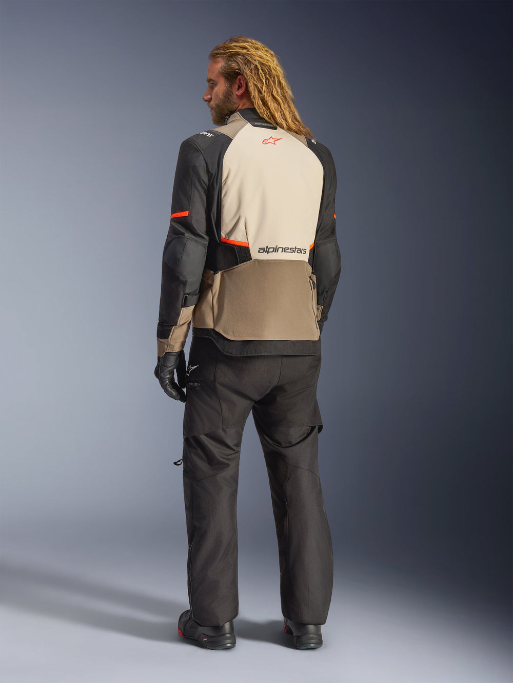 Alpinestars Andes V4 Drystar® Jacket, Walnut Mastic Black, rear view on male model, featuring tan and black reinforced textile panels with orange accents, Alpinestars logo on the back, worn with matching black adventure riding pants and gloves.