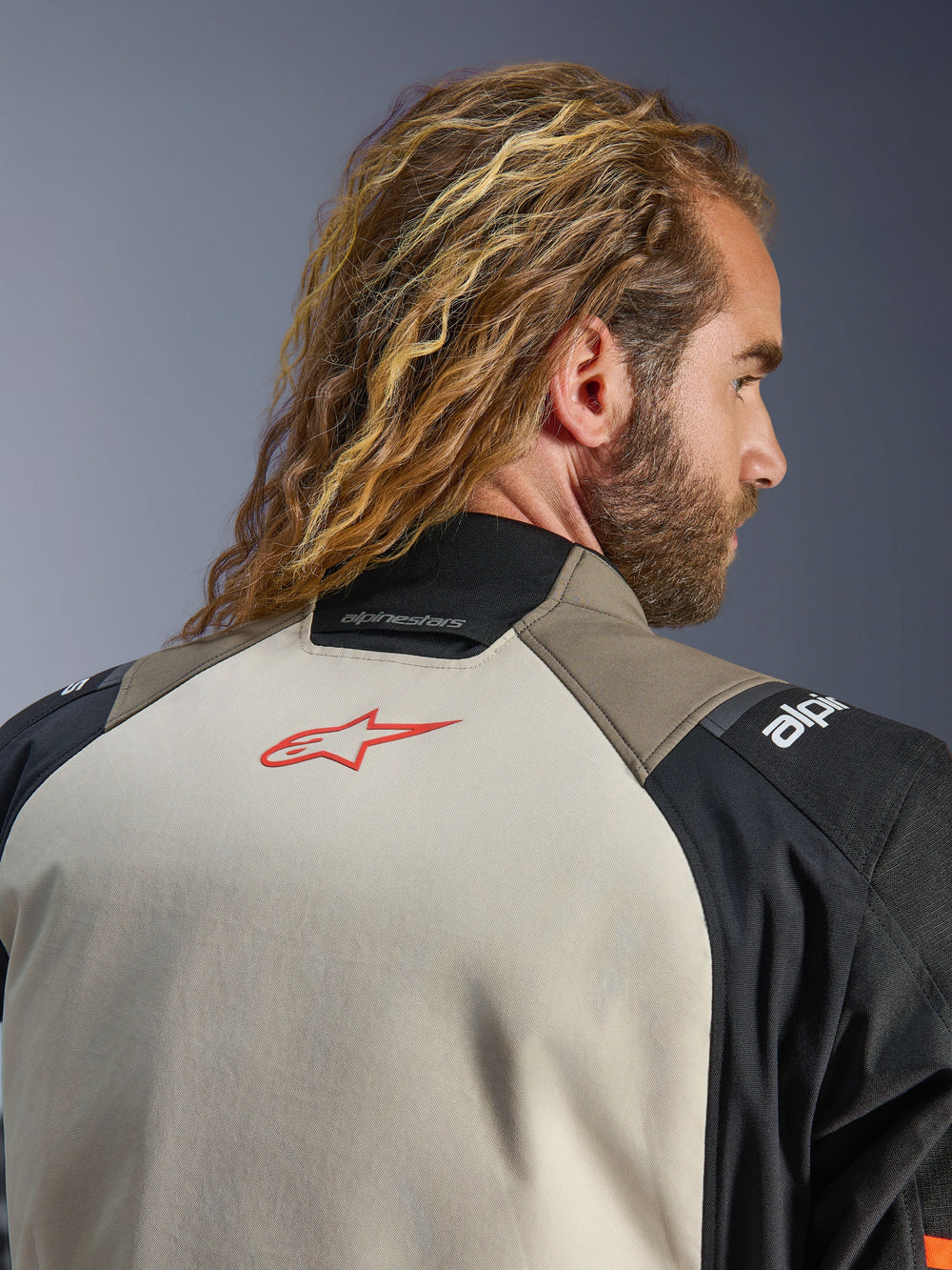 Alpinestars Andes V4 Drystar® Jacket, Walnut Mastic Black colorway, close-up view of the upper back and collar, featuring a red star logo on the mastic panel, walnut and black textile construction, adventure motorcycle touring gear