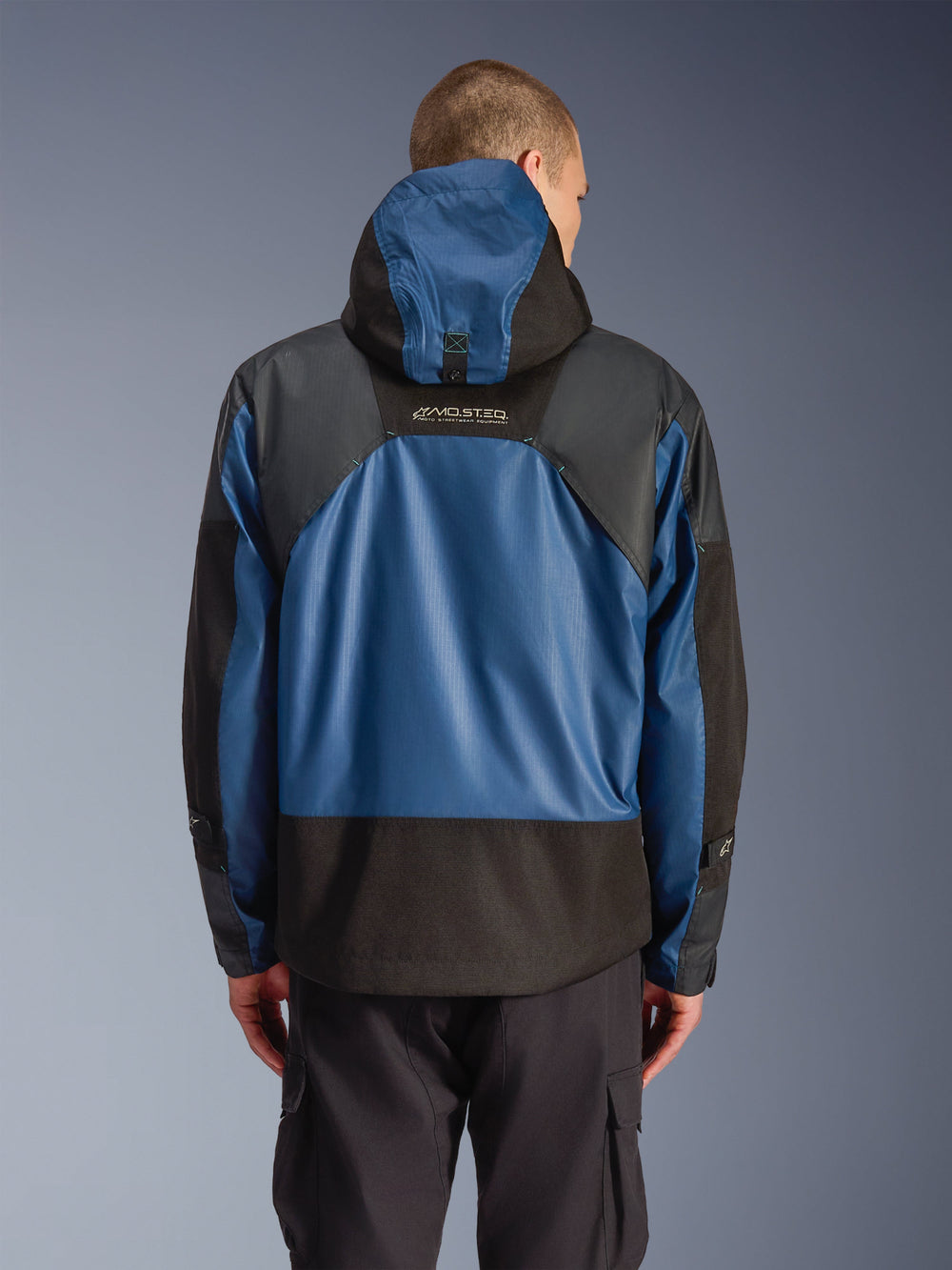 Alpinestars Mospher Waterproof Jacket in Black Dark Petrol, rear view of a motorcycle parka featuring blue ripstop panels and black reinforced sections, MO.ST.EQ. branding on the upper back, modern urban tactical design