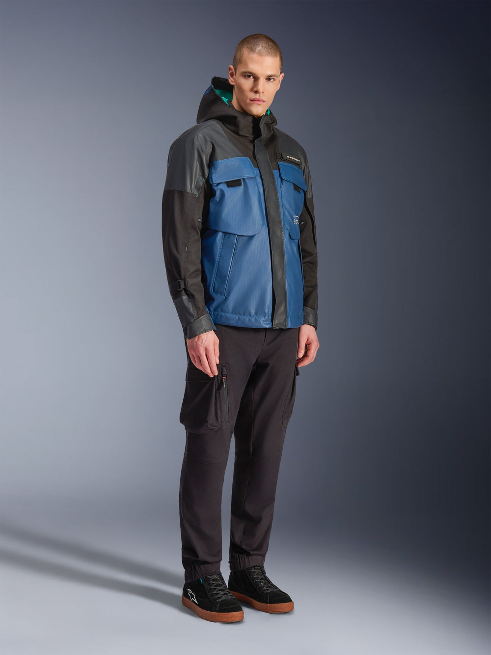 Alpinestars Mospher Waterproof Jacket, Black and Dark Petrol Blue, worn with black cargo pants and black sneakers, urban commuter style with utility pockets and hood