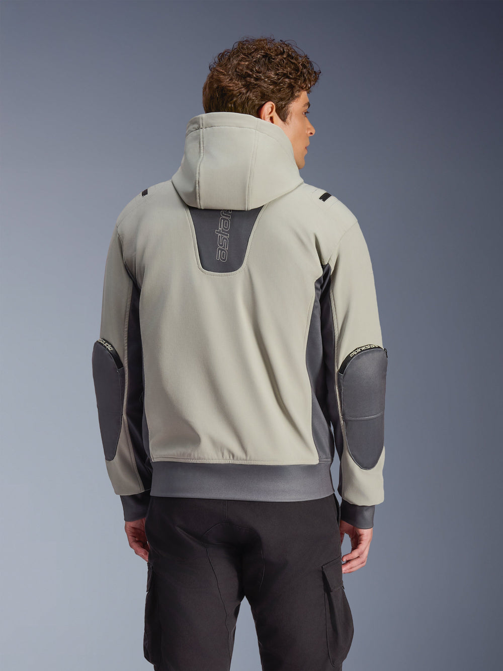 Alpinestars Moblast Waterproof Jacket in Iron Gray and Dark Sage, back view on model, hooded urban motorcycle jacket featuring dark gray stretch panels and reinforced elbows, paired with black cargo pants