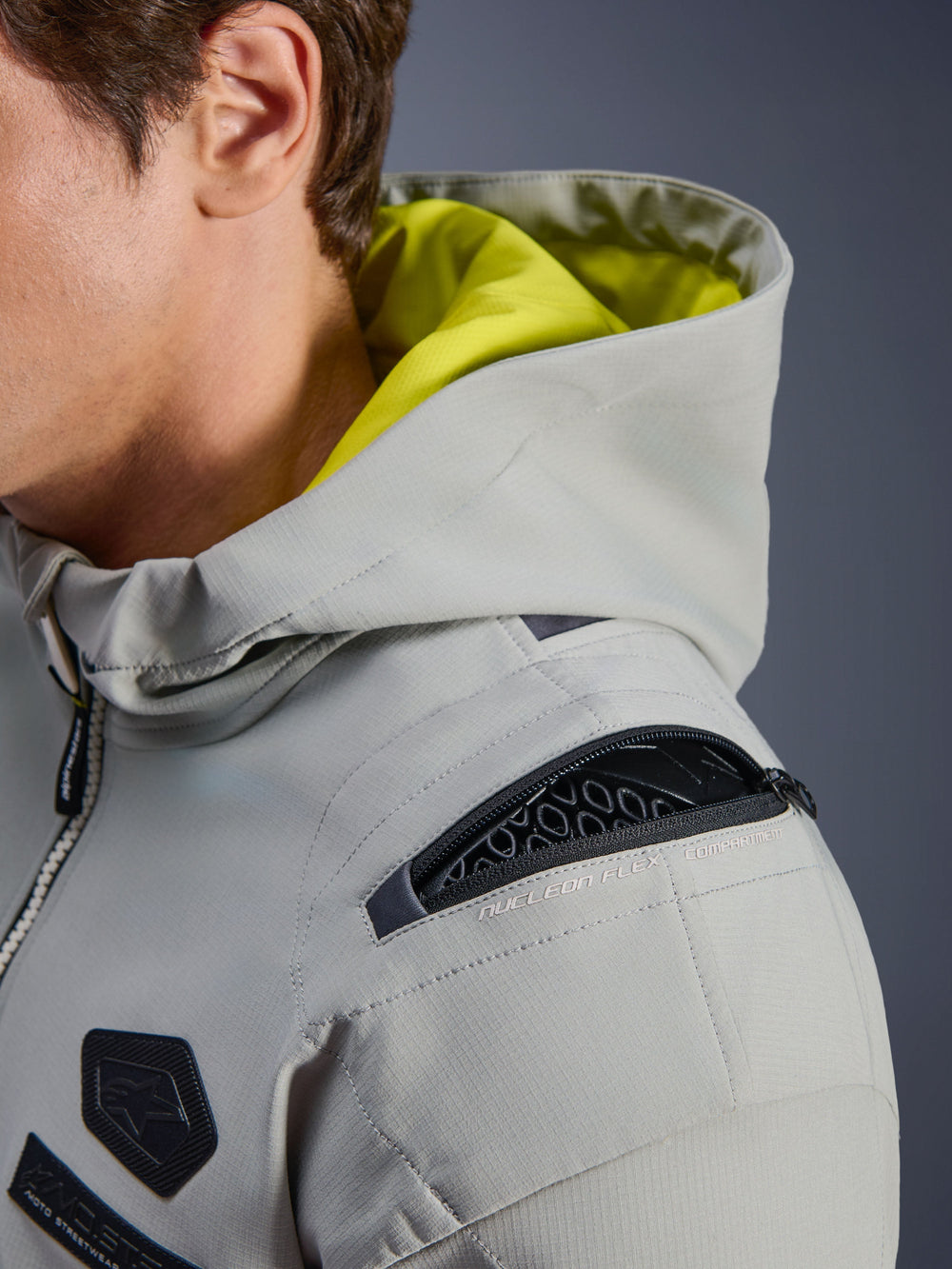 Alpinestars Moblast WP Jacket, Iron Gray, close-up of shoulder showing open Nucleon Flex protector compartment, neon yellow interior hood, technical urban motorcycle gear with functional zippers