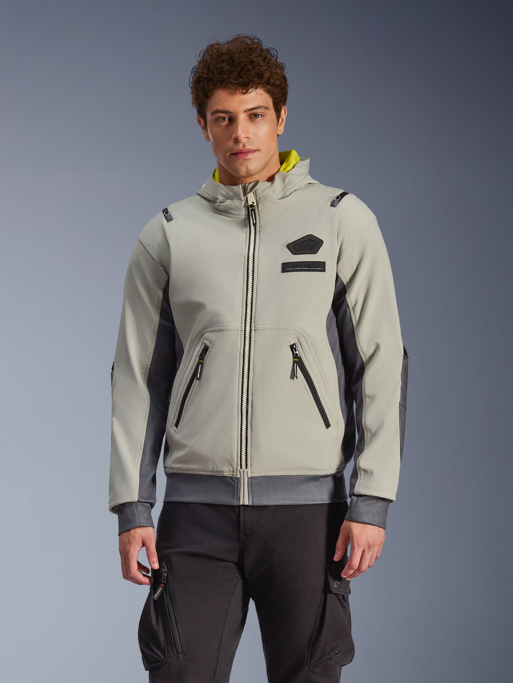 Alpinestars Moblast Waterproof Jacket, light gray and dark gray urban motorcycle hoodie with yellow hood lining, front pockets and black zippers, worn with black cargo pants, modern sporty design