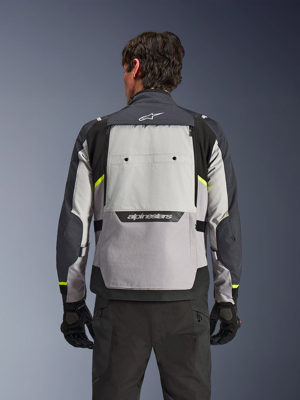 Rear view of a rider wearing the Alpinestars Cusco Drystar® Jacket in Ice Gray, Mid Gray, and Deep Gray, featuring neon yellow accents, a large back ventilation panel, and bold Alpinestars branding, paired with black riding pants and gloves.