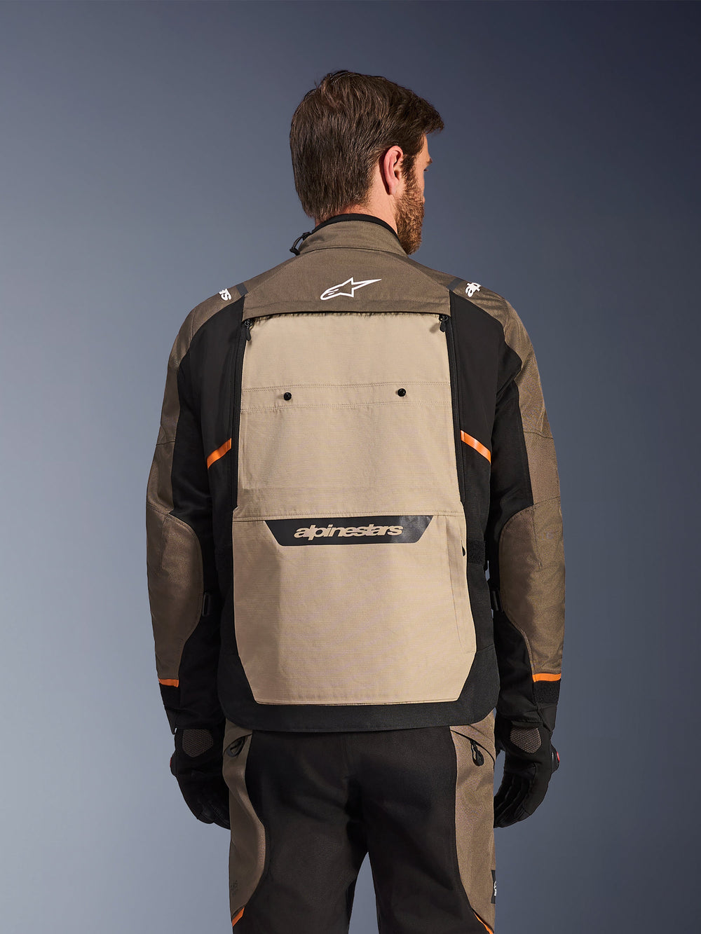 Alpinestars Cusco Drystar® Jacket, Walnut Aluminum Black, rear view, featuring a large tan back panel with black logo, orange accents, worn with matching pants and gloves, designed for adventure touring.