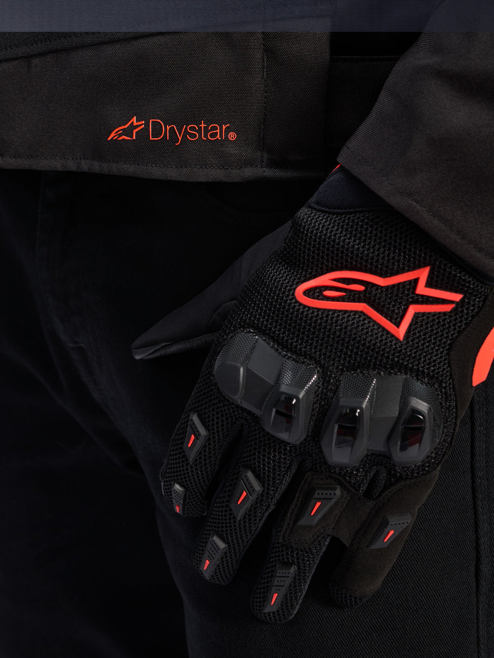 Close-up of the Alpinestars T-GP R V3 Drystar® Jacket waist featuring a red Drystar logo, shown with a black motorcycle glove with a red Alpinestars star logo, mesh fabric, and reinforced knuckle protection.