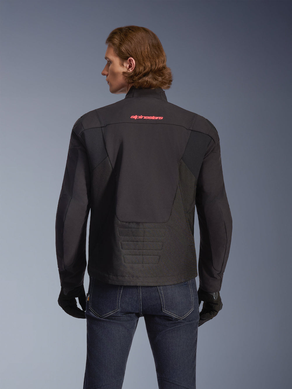 Alpinestars SMX Waterproof Jacket, Black with Bright Red logo, rear view shown on a model, worn with dark blue jeans and black gloves, textile motorcycle jacket for road and sport riding.