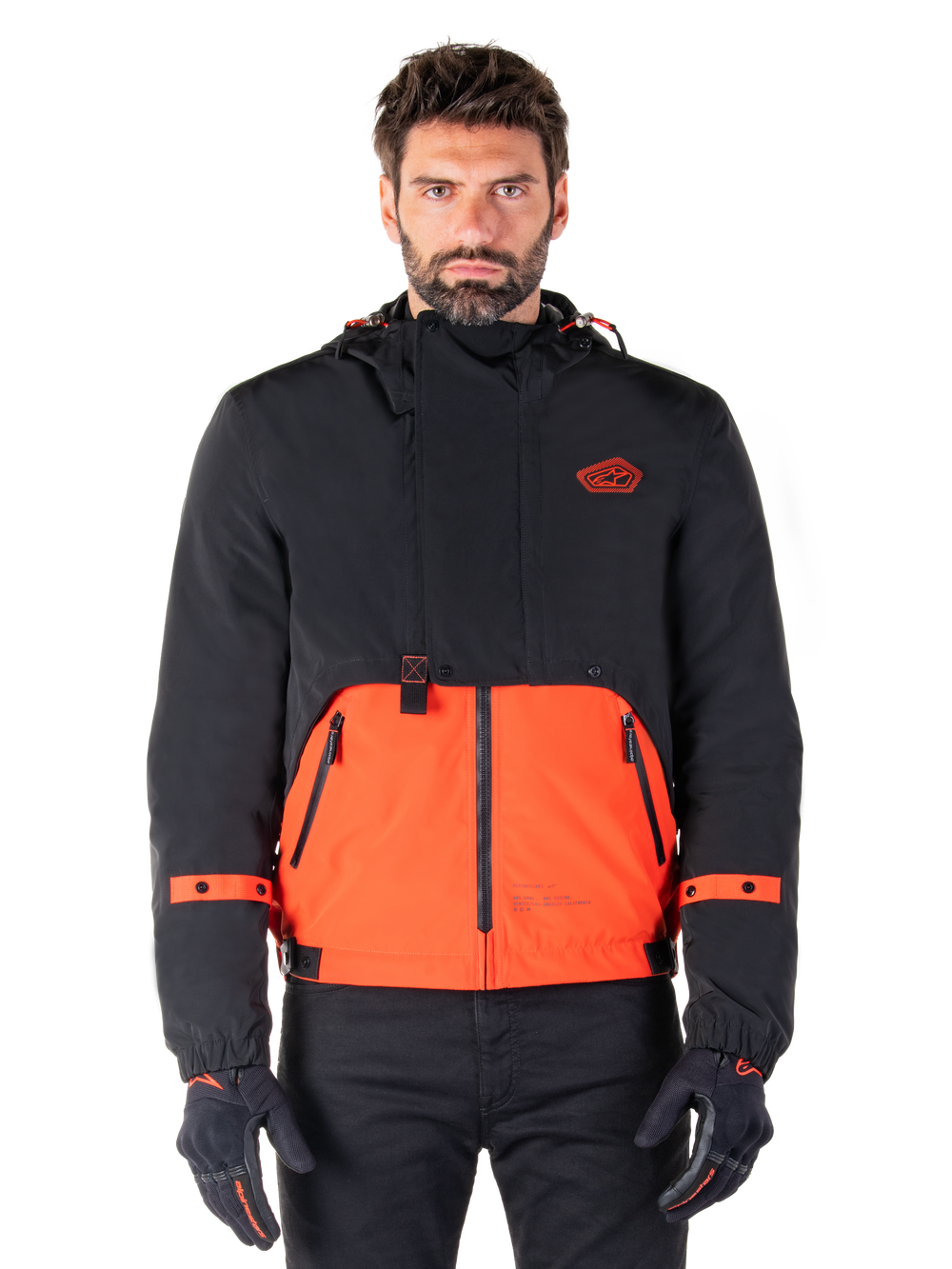 Alpinestars Mootant Waterproof Parka, modular motorcycle jacket in Spicy Orange and Black, worn by a model with matching gloves, features a hooded design with two-tone panels, front zipper, and adjustable cuffs, urban contemporary riding apparel