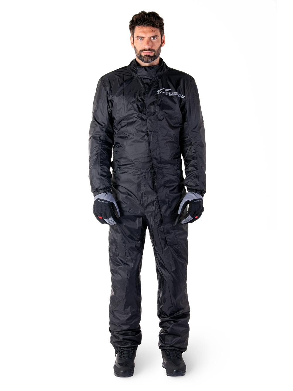 Alpinestars Hurricane Rain V2 Suit, Full-Body Motorcycle Rain Suit in Black, waterproof protective gear with high collar and front storm closure, featuring white logo on chest, worn with black and grey gloves and boots