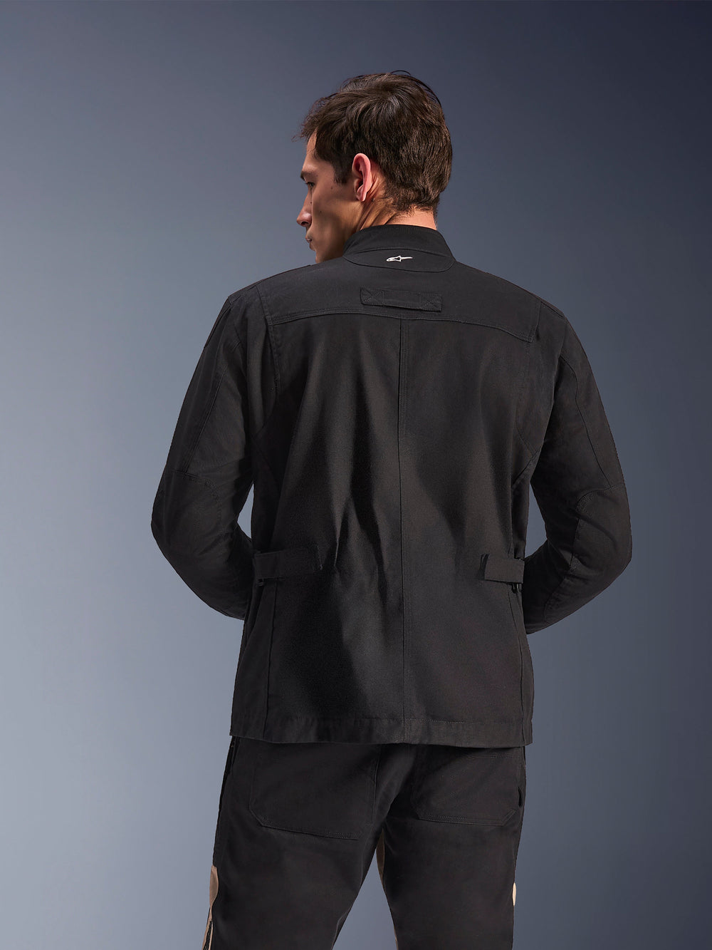 Alpinestars Dice Jacket, Urban Motorcycle Jacket, Black, back view showing pleated shoulders and adjustable waist tabs, field jacket aesthetic with small white logo on collar, protective textile gear for city riding