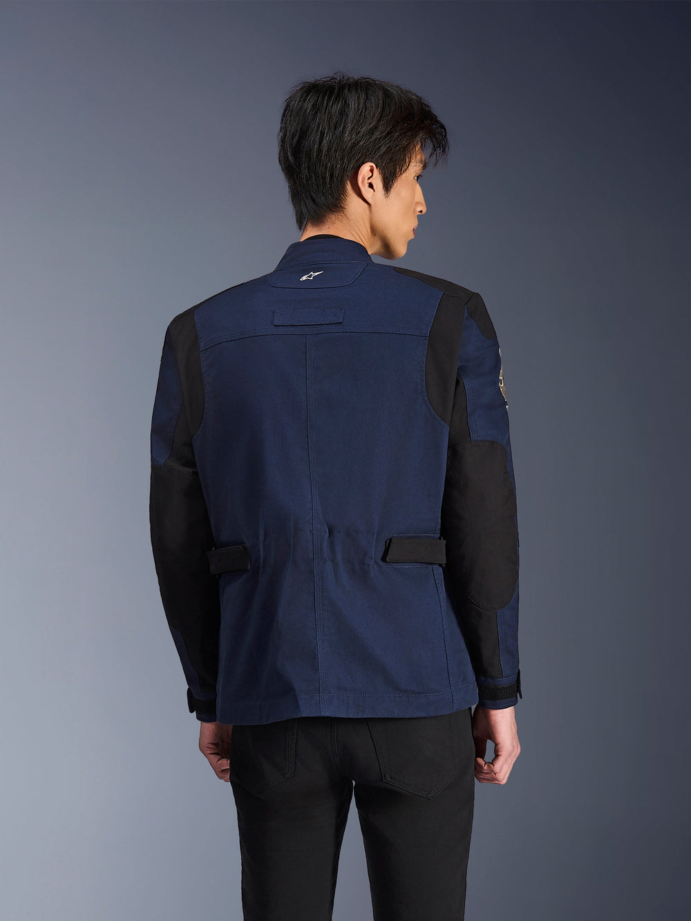 Alpinestars Dice Jacket, Dark Blue and Black urban field motorcycle jacket, back view worn by a man, featuring reinforced black shoulder and elbow panels with adjustable waist tabs.