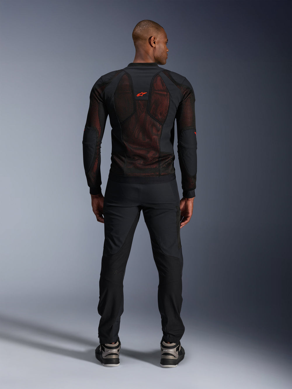 Alpinestars Troop-Air Pro Jacket in Black Red Fluo, rear view on model, technical armored mesh jacket with breathable panels, red logo on upper back, worn with black pants and sneakers, urban motorcycle apparel