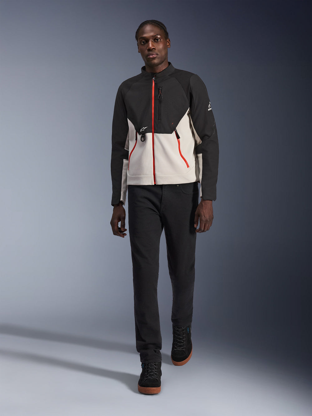 Male model wearing the Alpinestars Provoke Jacket, urban motorcycle jacket in black and metal gray with red zipper accents, paired with black pants and black high-top shoes, modern street-ready protective gear for city riding