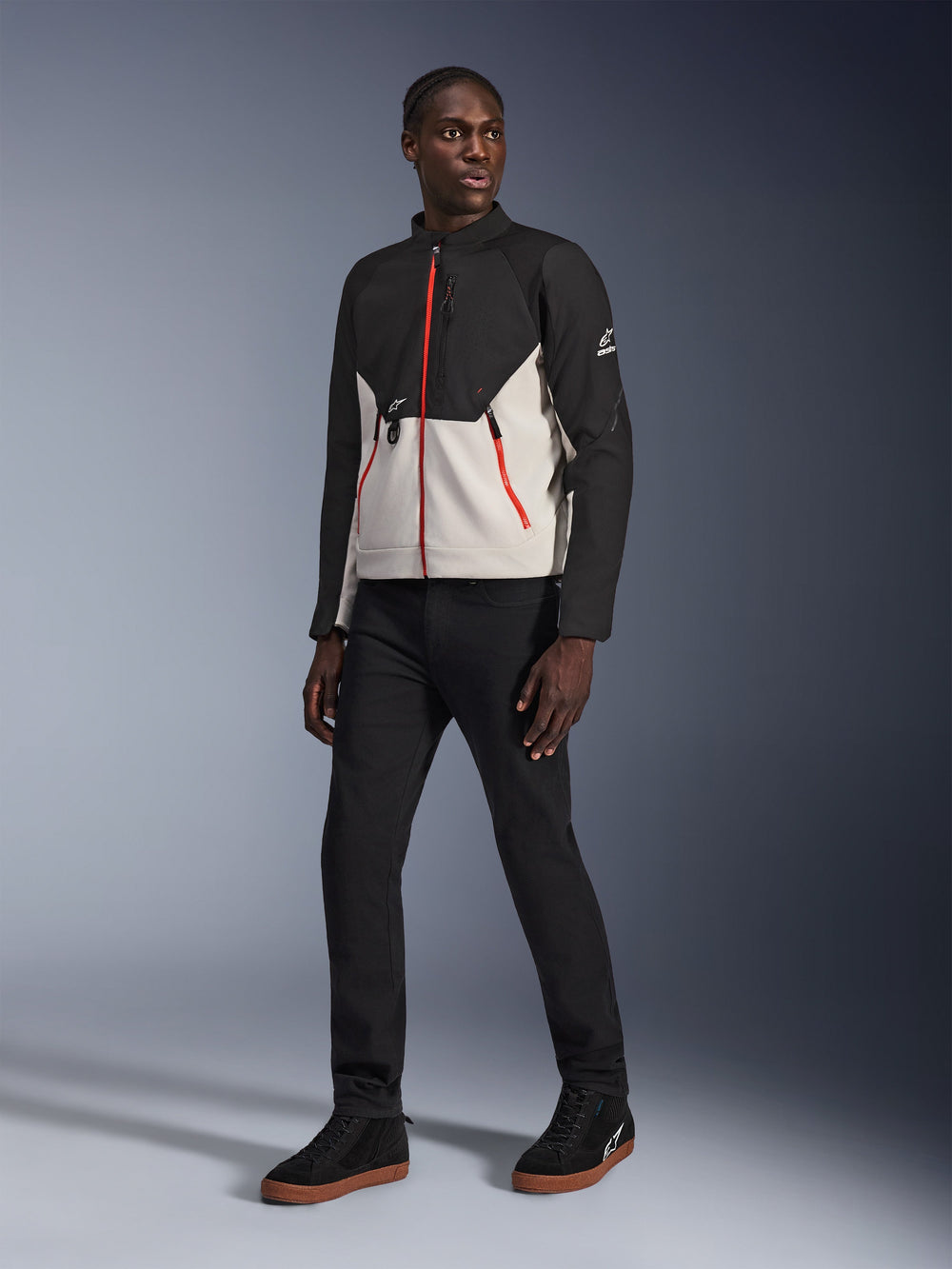 Model wearing the Alpinestars Provoke Jacket in Black Metal Gray, featuring distinctive red front and pocket zippers, paired with black pants and black high-top sneakers with gum soles, urban contemporary motorcycle gear for a street-ready look.