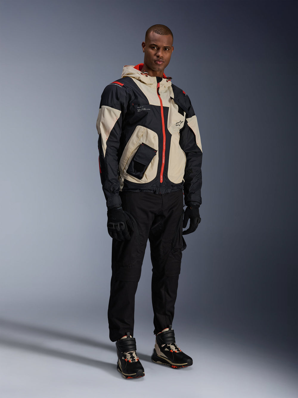 Man standing in full urban motorcycle gear, featuring Alpinestars Speedstreet Shoes in Black Almond Hot Orange and a Mogress Air Jacket in black and cream, coordinated black pants and gloves, streetwear-inspired protective outfit for street riding
